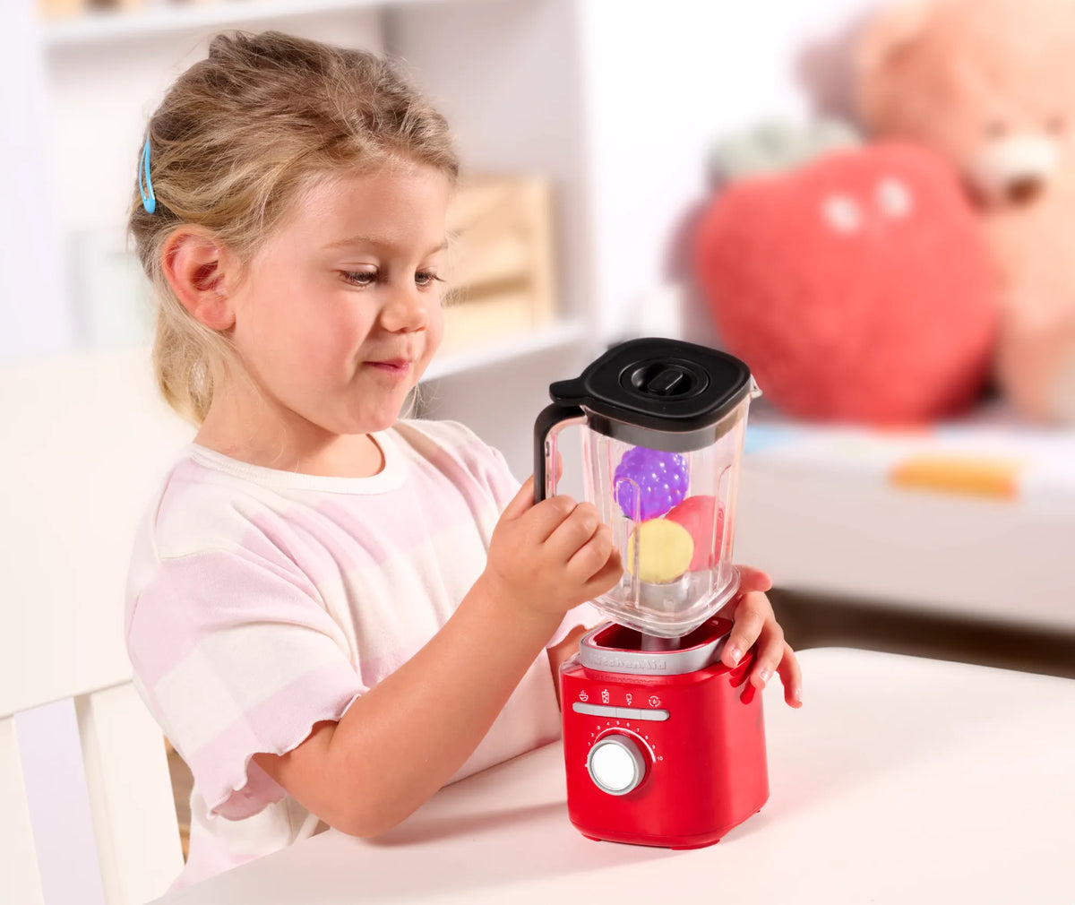A girl blending toy fruit in a KitchenAid Kids blender