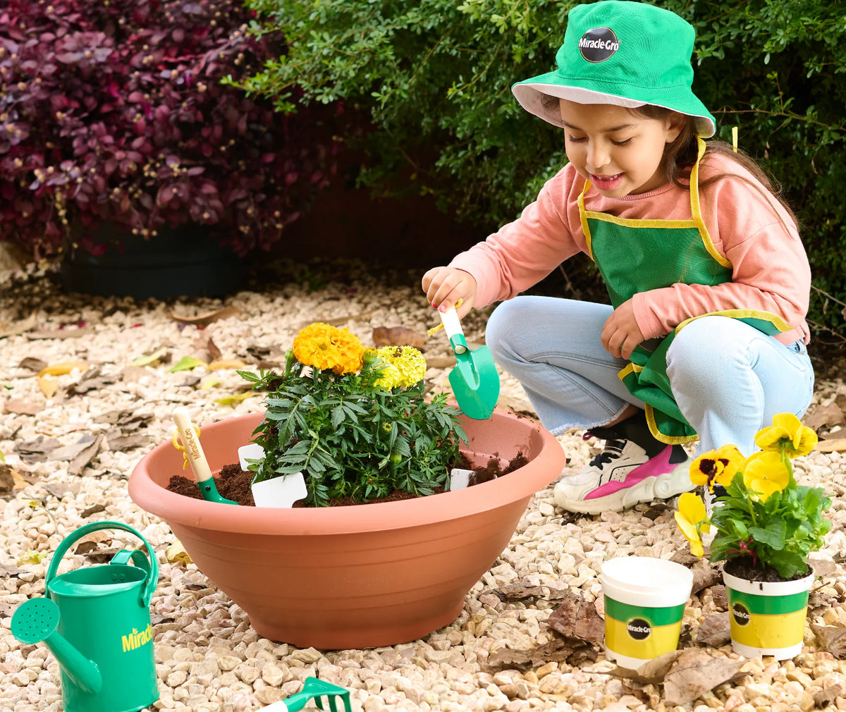 A girl planting yellow flowers with Miracle-Gro Kids garden tools