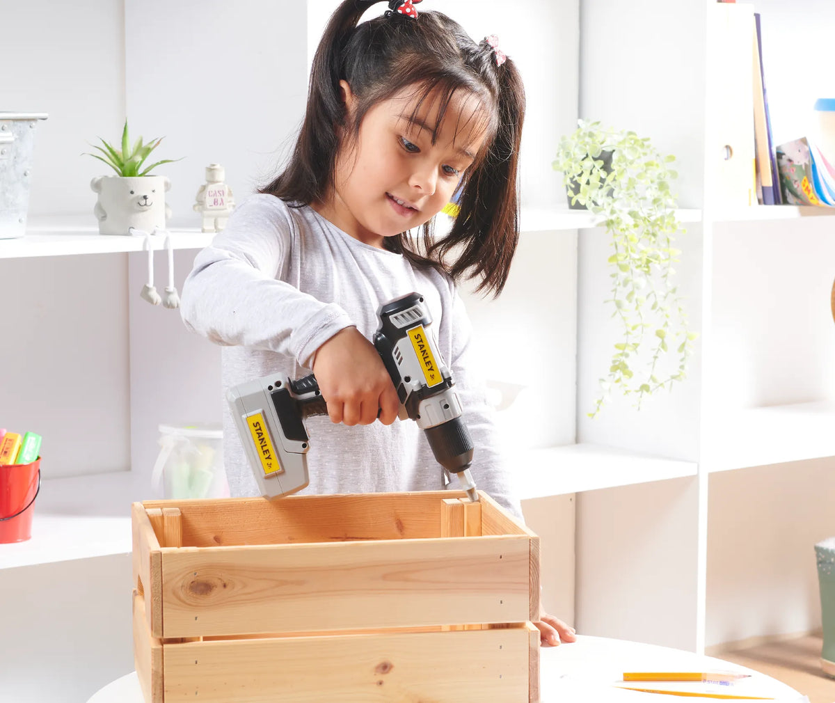 A girl drilling into a wooden crate with a STANLEY Jr. toy drill