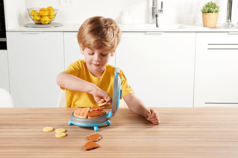 A child using a toy drill on a wooden crate with an adult nearby