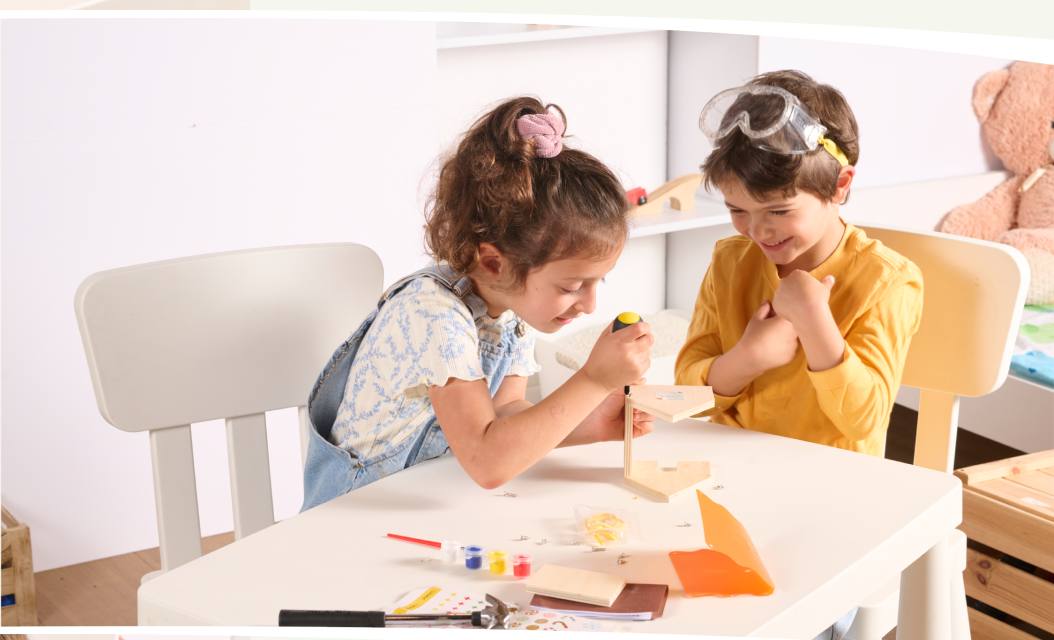 Two children painting and hammering a wooden craft kit together at a table.